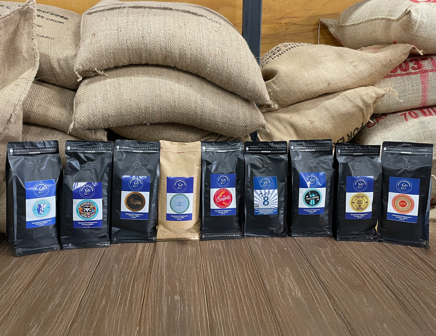 Row of specialty coffee bags with visible Art of Espresso branding on a wooden surface, with burlap sacks in the background.